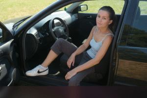 Mulher loira sentada numa viatura com ar introspectivo e casual. Sou Alberta do clube dos pecados